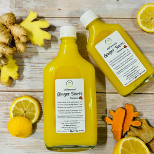 TWO BOTTLES OF TURMERIC GINGER SHOTS WITH FRESH PICES OF TURMERIC LEMON AND GINGER