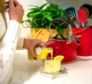 Girl on white sweater is pouring fresh pineapple ginger honey lemon shots into hot water a making hot ginger tea
